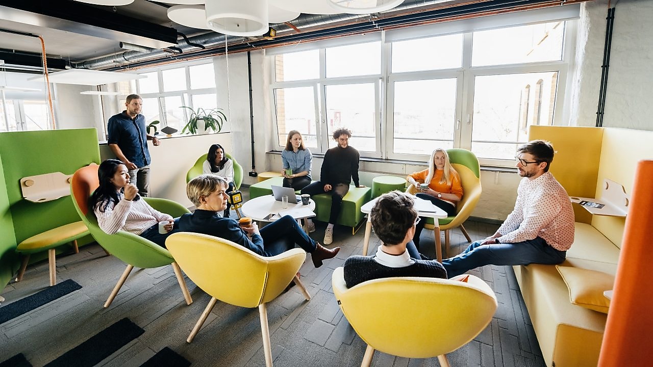 Grup de tineri colegi discutând într-o sală de ședințe cool dintr-o clădire de birouri modernă.