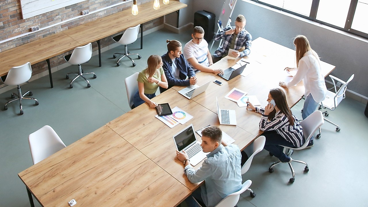 Întâlnire între colegi de birou tineri și vibranți care are loc într-o sală modernă. Fiecare participant are un laptop, o tabletă sau grafice pregătite