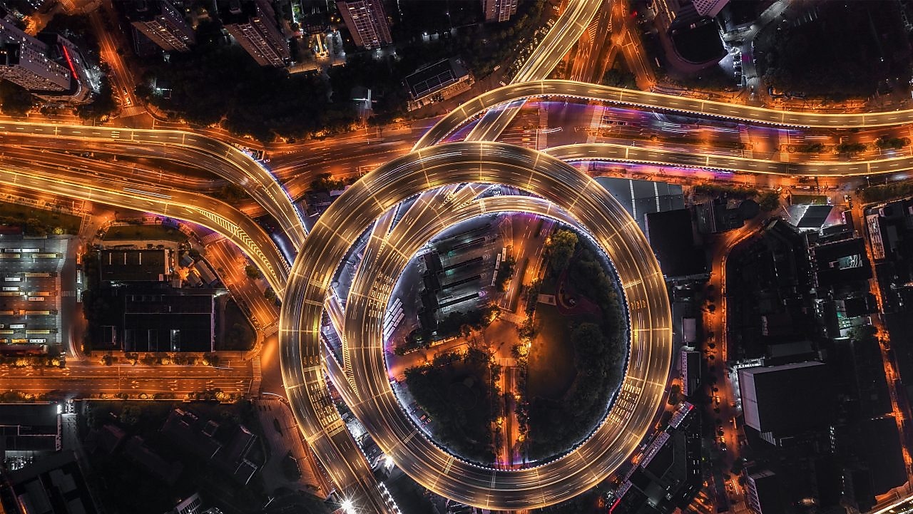 Nod rutier circular cu autostrăzi suprapuse și iluminate artificial, văzut de sus, noaptea.