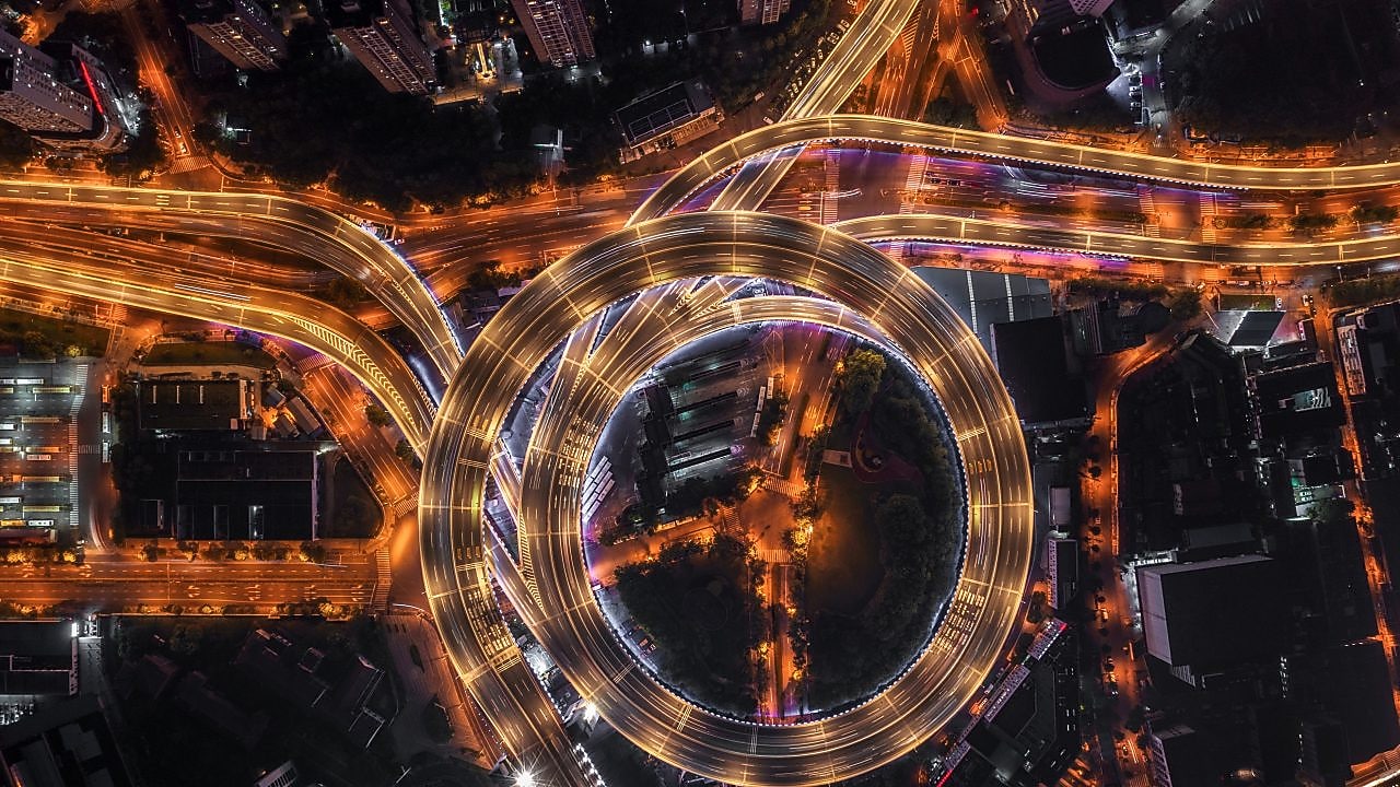 Nod rutier circular cu autostrăzi suprapuse și iluminate artificial, văzut de sus, noaptea.