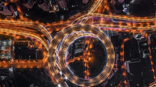 Nod rutier circular cu autostrăzi suprapuse și iluminate artificial, văzut de sus, noaptea.