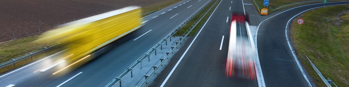 Două tiruri se deplasează pe o autostradă pe timpul unui frumos apus de soare; imaginea lor este ștearsă din cauza mișcării