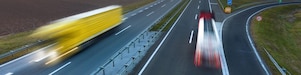 Două tiruri se deplasează pe o autostradă pe timpul unui frumos apus de soare; imaginea lor este ștearsă din cauza mișcării